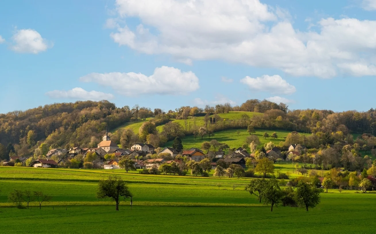 Le village de Présilly en Haute-Savoie, avec son église au pied de coteaux boisés et la campagne genevoise environnante
